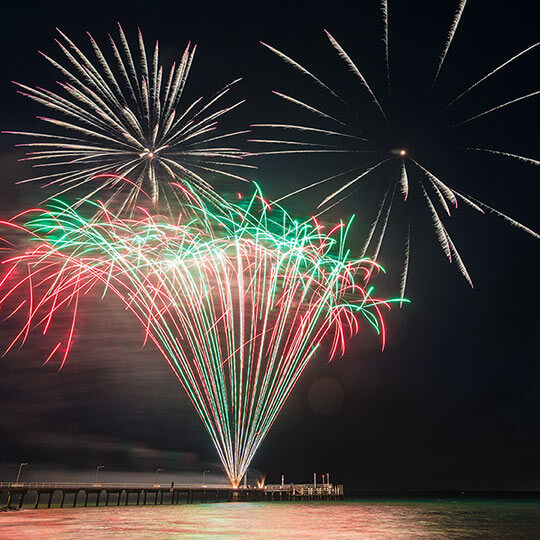 Large fireworks display over the water in red and green.