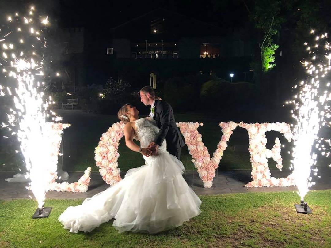 Bridal couple in front of Love sign and fireworks.